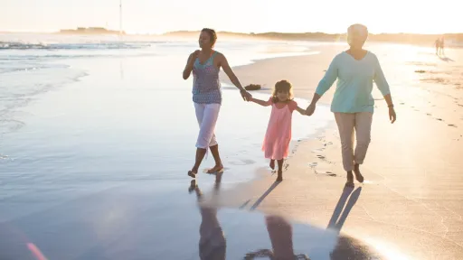 Grandmother, her daughter and her grand daughter walking along together on the beach at sunset