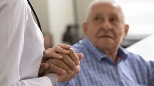 Helping hands. Close up of kind compassionate female doctor nurse in white coat supporting soothing consoling aged retired man patient. Focus on sick old man palm in hands of medical worker caregiver