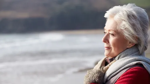 Senior Woman Walking On Winter Beach Looking Off Camera