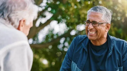 Attractive middle aged Caucasian woman with loose gray hair and wrinkles spending day indoors, leaning on white wall and smiling at camera.