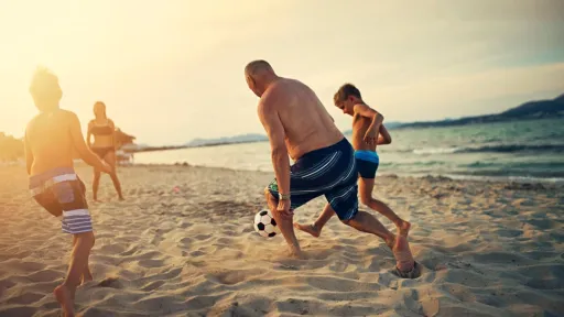 Three kids playing soccer with grandfather. The boys are aged 8 and girl is 13.  Family is enjoying sunny summer day on beach. Nikon D850