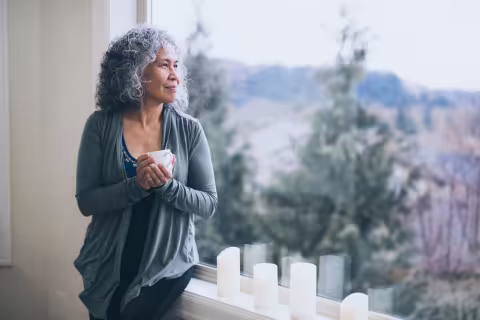 Mature and vibrant Hawaiian woman stands by her window in the early morning and contemplates the mysteries of the universe.